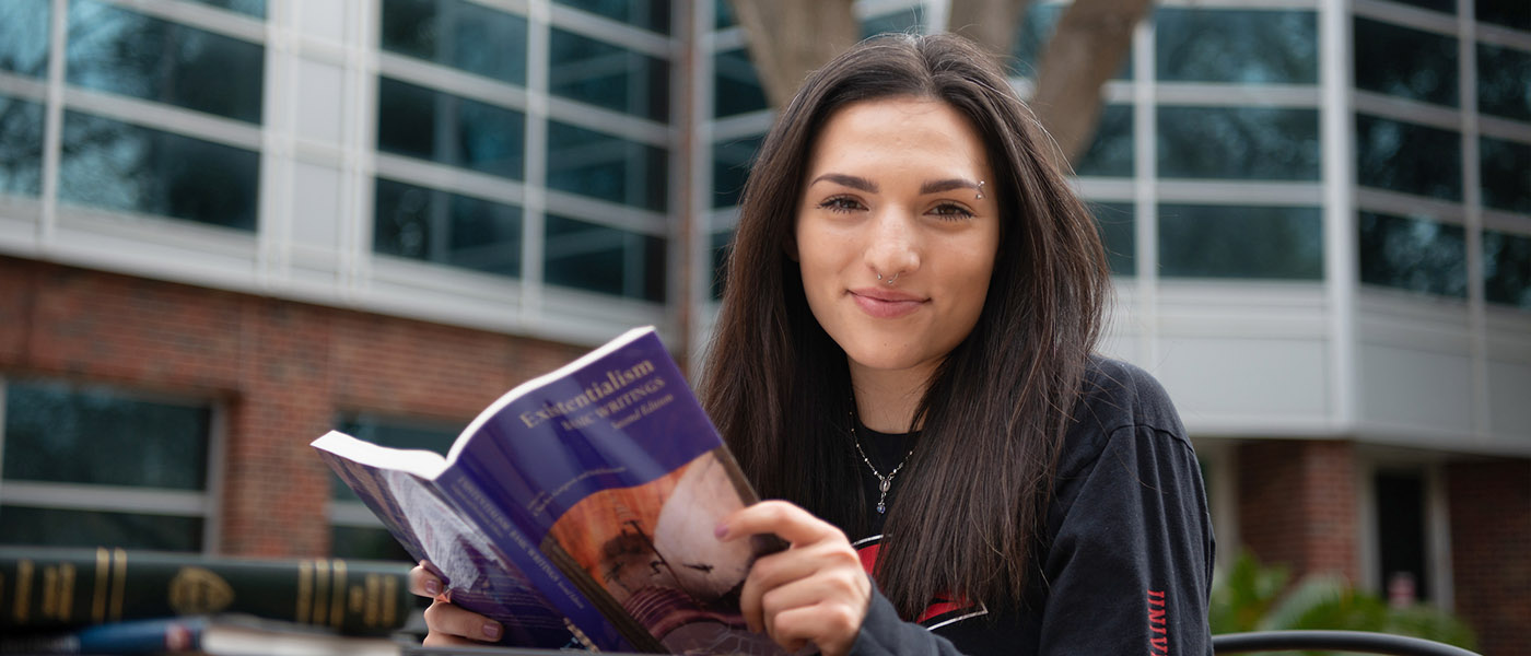Philosophy student sitting on outdoor table in front of the library reading a book
