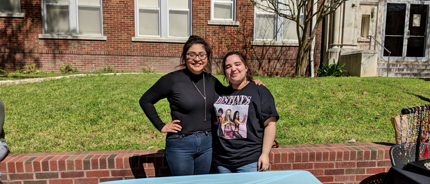 Two smiling women's studies students recruiting members for a club in the courtyard