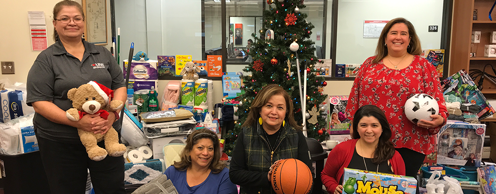 Rosenberg School of Optometry staff pose in front of a Christmas tree surrounded by gifts