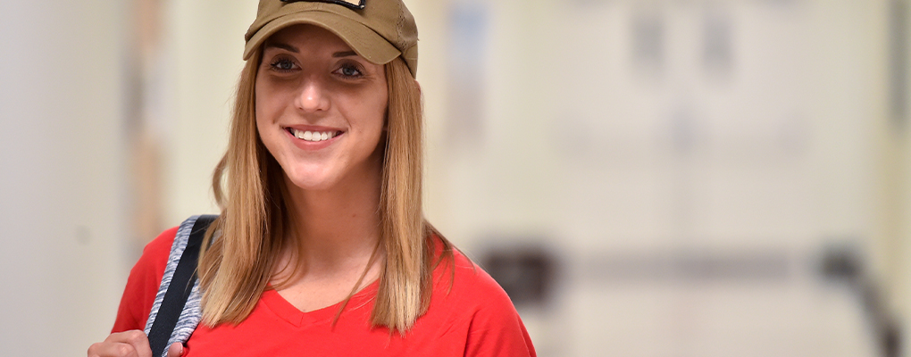 A student wearing a baseball cap smiles at the camera
