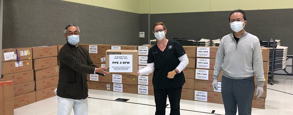 Three people in surgical masks pose for a photo in front of boxes of ppe