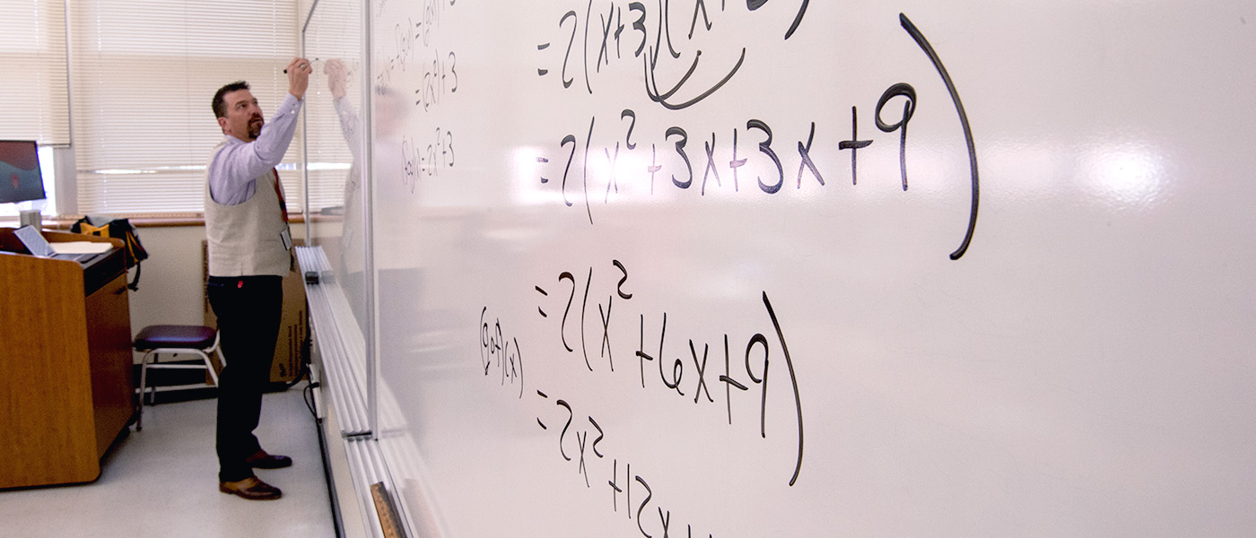 Mathematics professor working on equations on whiteboard during class