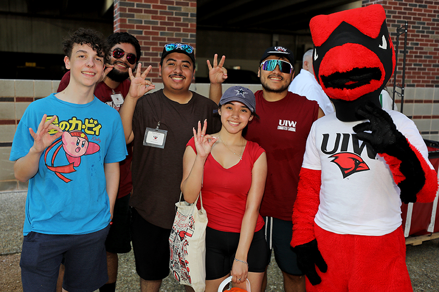 Students making the Cardinal hand sign with mascot Red the Cardinal