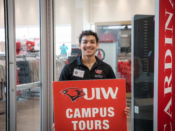 student holding a sign reading UIW campus tours