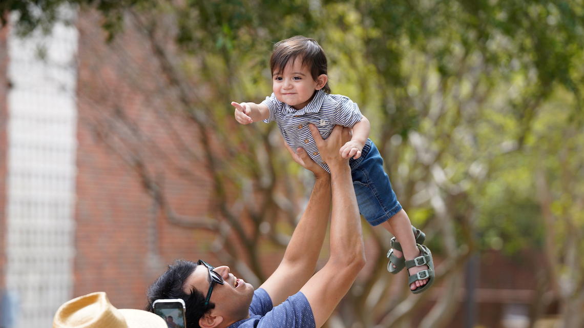 Parent holds his child in the air at Homecoming event