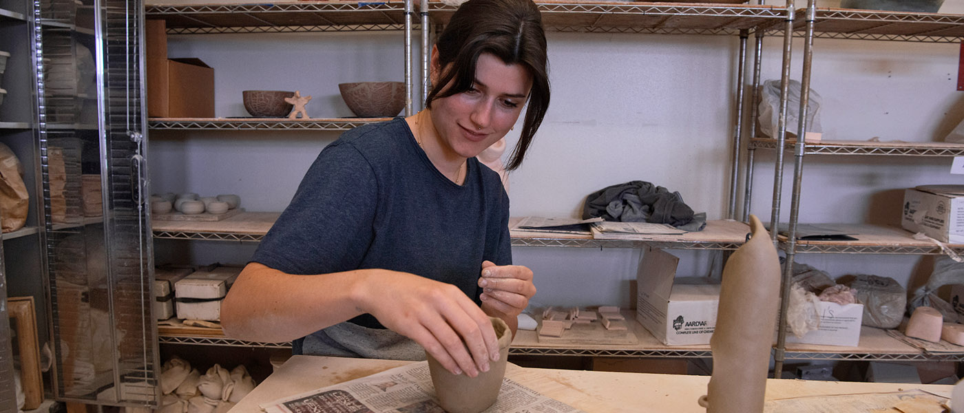 Smiling art student looking at the camera as she paints a ceramic project with glaze