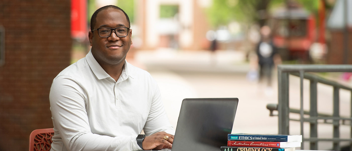 Criminal justice student sitting at an outdoor table on campus using his laptop