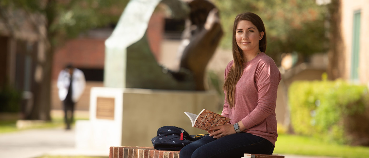 English student reading a book outside on campus courtyard