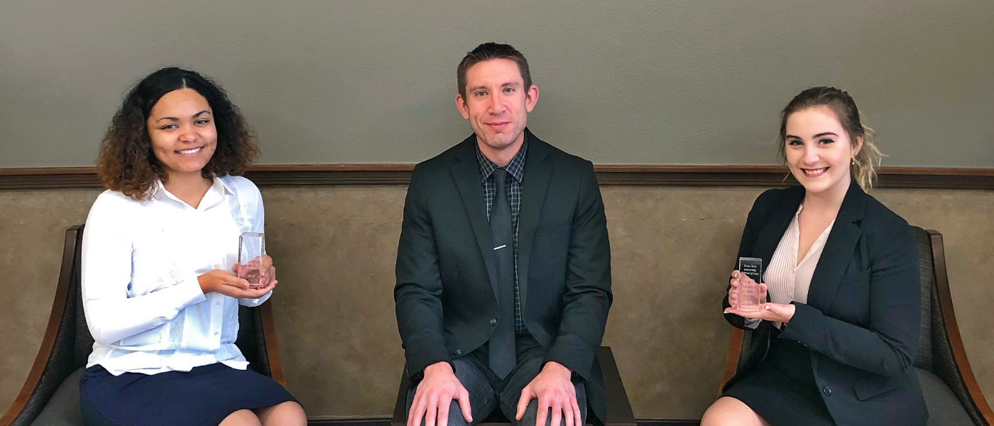 Three political science students sitting in courthouse lobby holding up awards