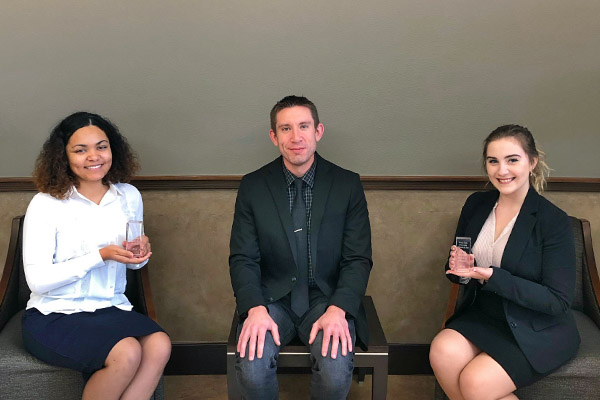 Three political science students sitting in courthouse lobby holding up awards