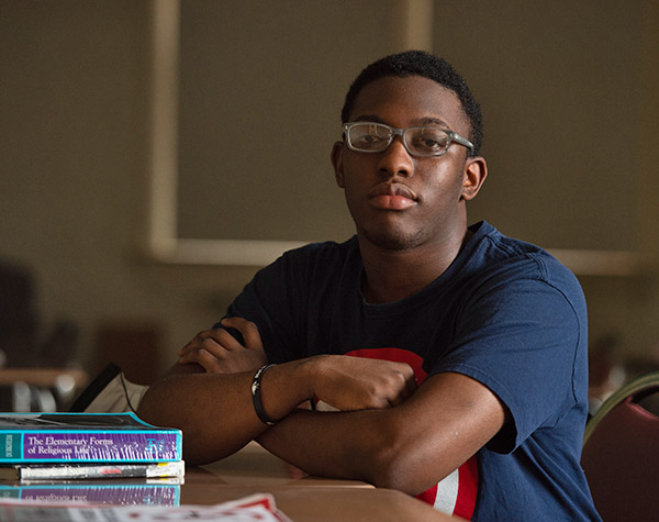 Sociology student in a classroom sitting in a desk with a few books