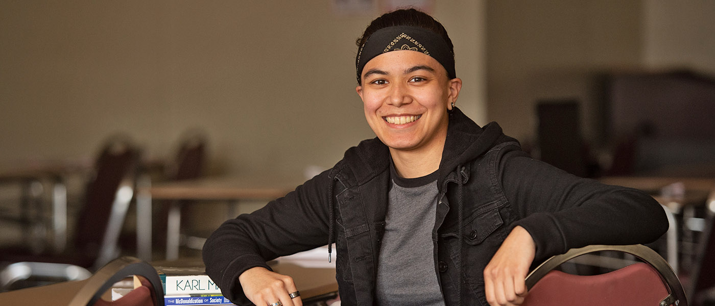 Smiling sociology student sitting in a desk with a few books on it