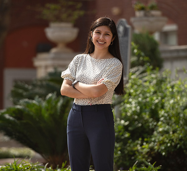 Smiling student posing with her arms crossed in front of the administration building