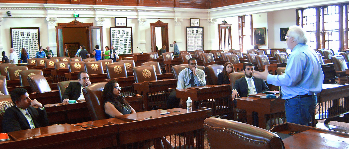 Students sitting in the local house of representatives floor as a professor gives a lesson on the legislative process