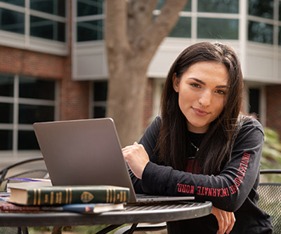 Student with books and laptop studying outside in the library courtyard