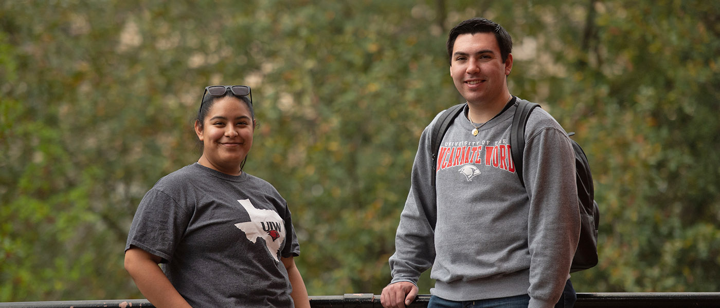 Two smiling students standing outside with trees in the background