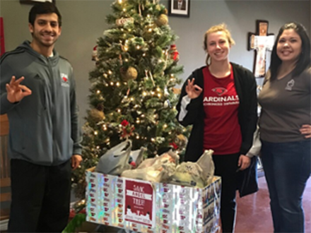 3 student athletes posing around a christmas donation box