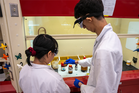 Student wearing safety equipment holding a small vial