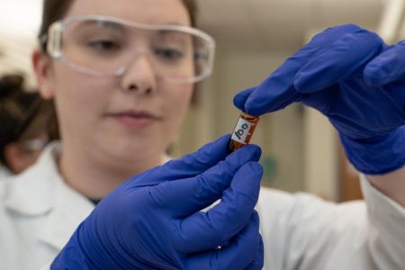 Student wearing safety equipment holding a small vial