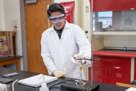 Student wearing a lab coat and safety gear conducting a chemistry experiment in a laboratory