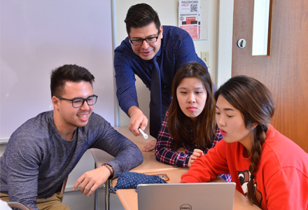 4 MHA students gathered around a computer, working on something together.