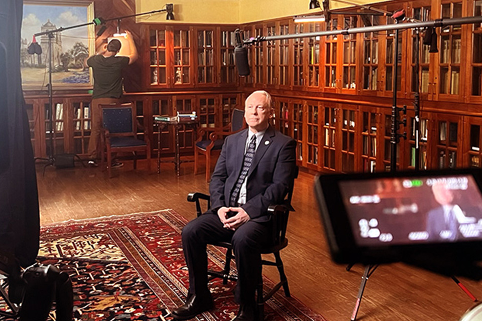 Faculty being interviewed sitting on chair with cameras around