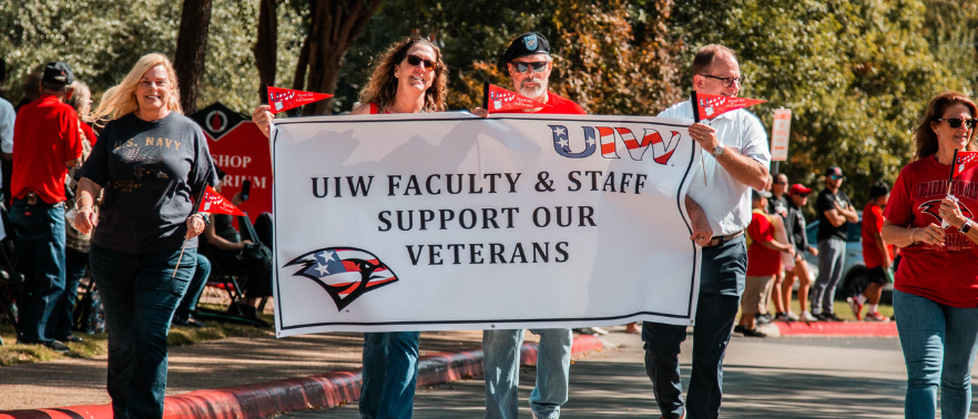 Four UIW faculty members marching in Veterans Day Parade holding a banner that says UIW Faculty and Staff Support Our Veterans