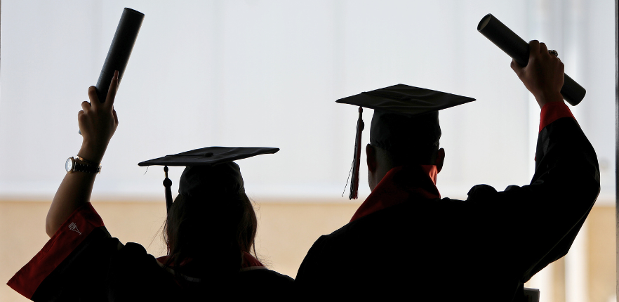 Two UIW graduates facing away from the camera, holding up diplomas in celebration