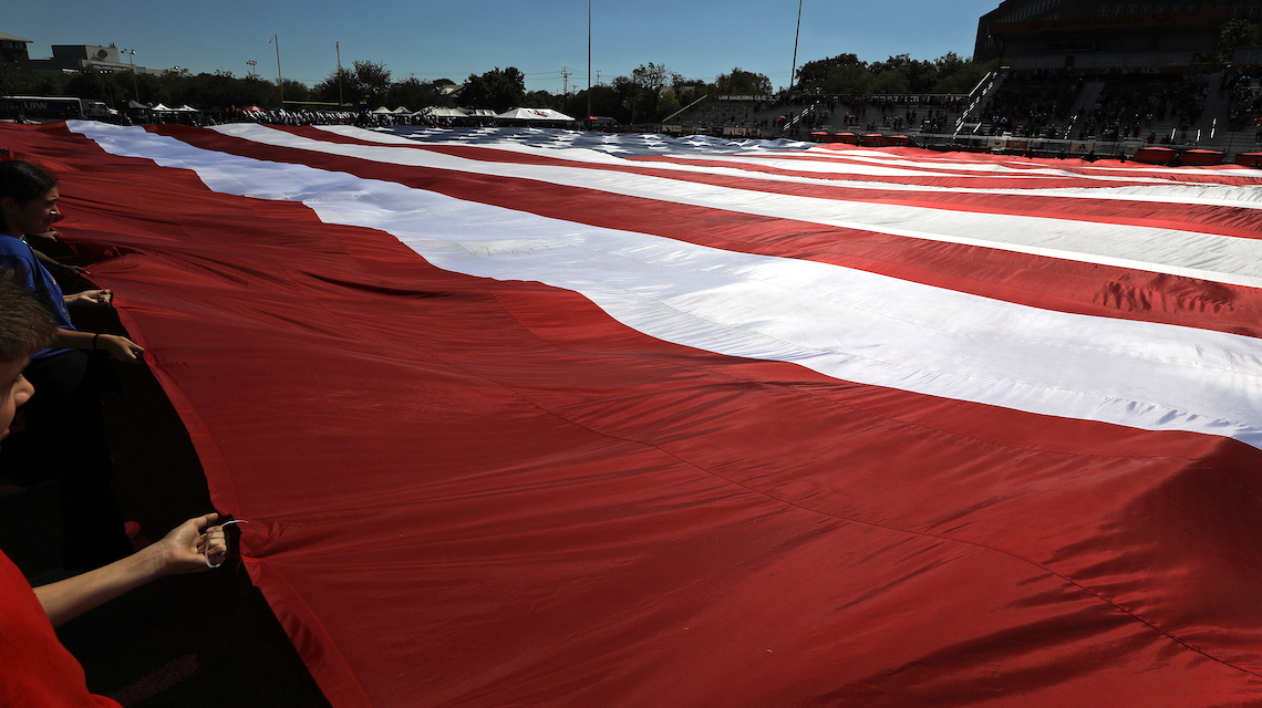 Ground-level shot of the field sized American flag being held by local ROTC and JROTC units 