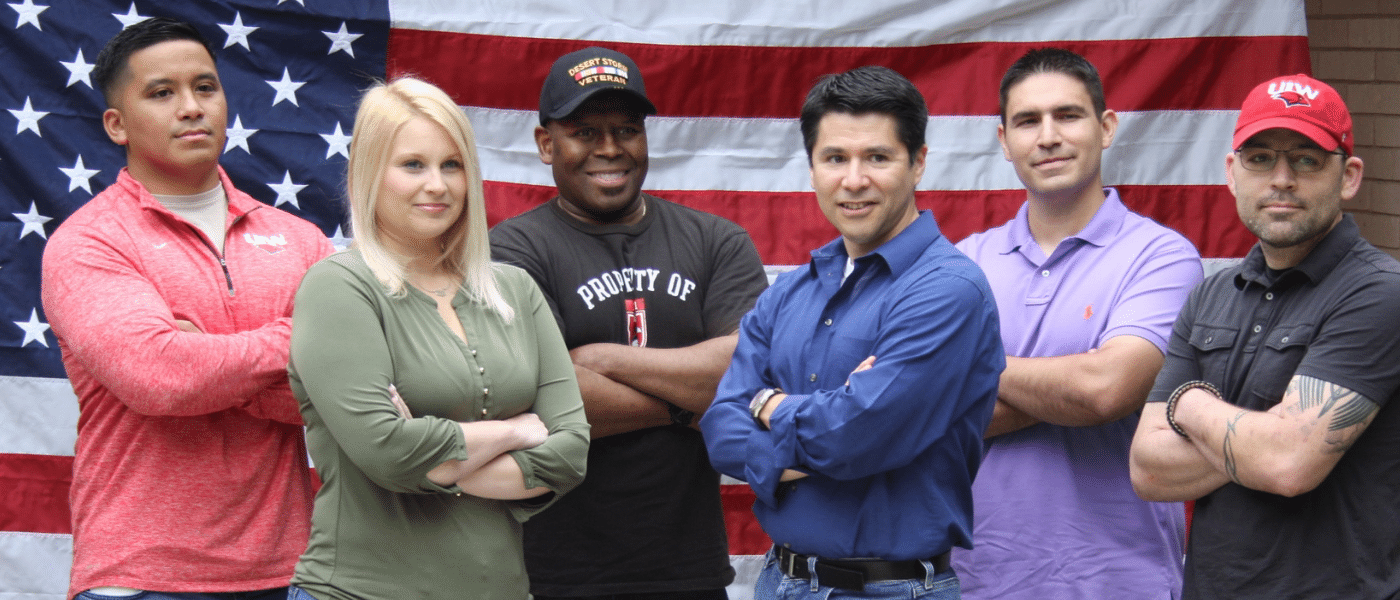 Group of veteran students standing in front of the U.S. flag with their arms crossed.