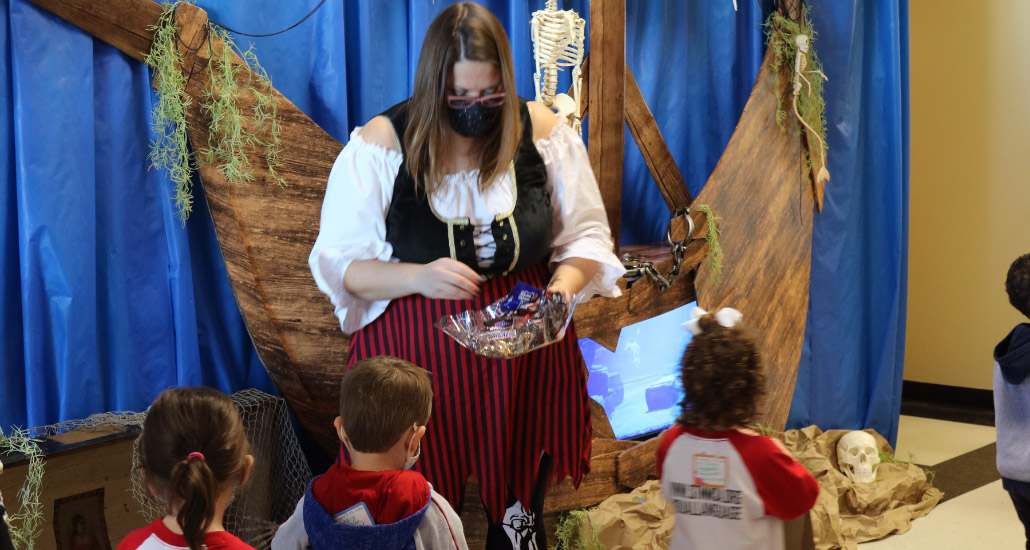 Woman dressed as pirate giving Halloween candy to children