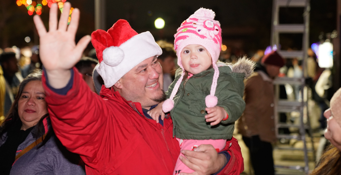 Man waves while holding daughter, who is wearing a pink hat