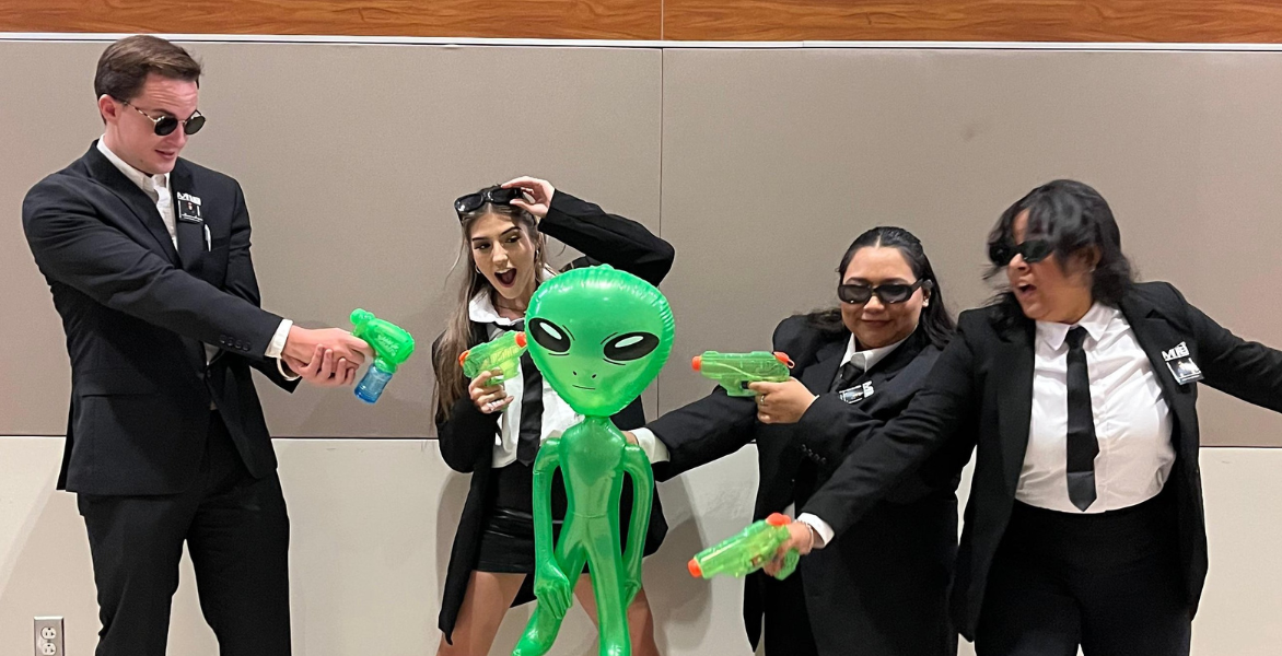 Students dressed as Men in Black members holding a green alien