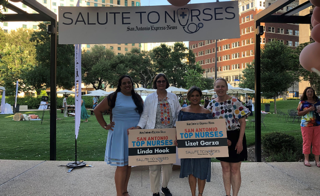 Four women smile in front of a Salute to Nurses sign