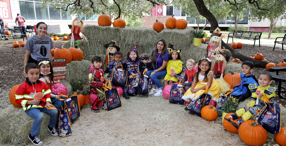 Young children dressed up for Halloween sitting on hay bales