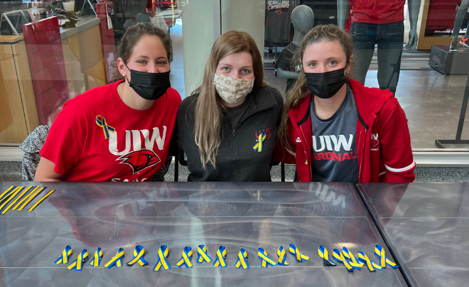 Three student-athletes volunteer to hand out blue and yellow ribbons