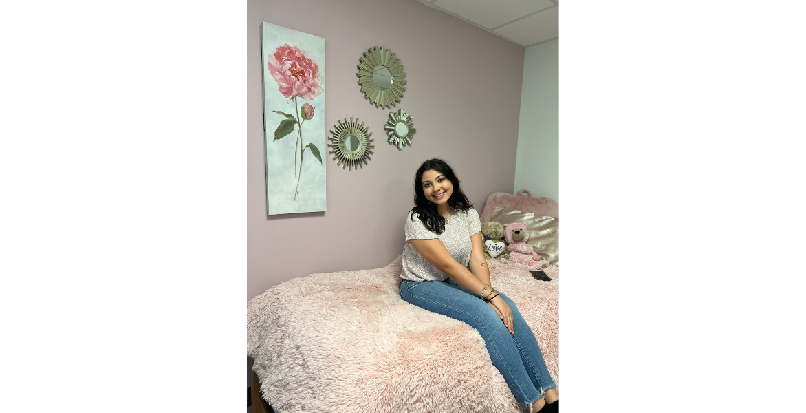 Student smiles while sitting on their bed after moving into the dorm