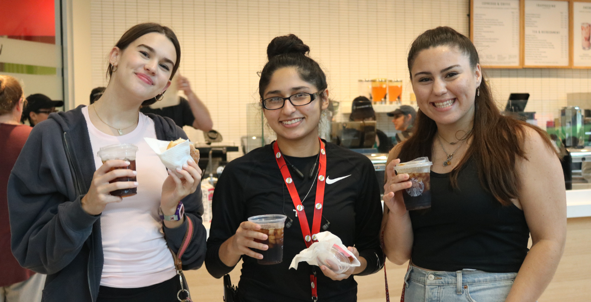 Three students pose with Starbucks at a Coffee and Donuts event
