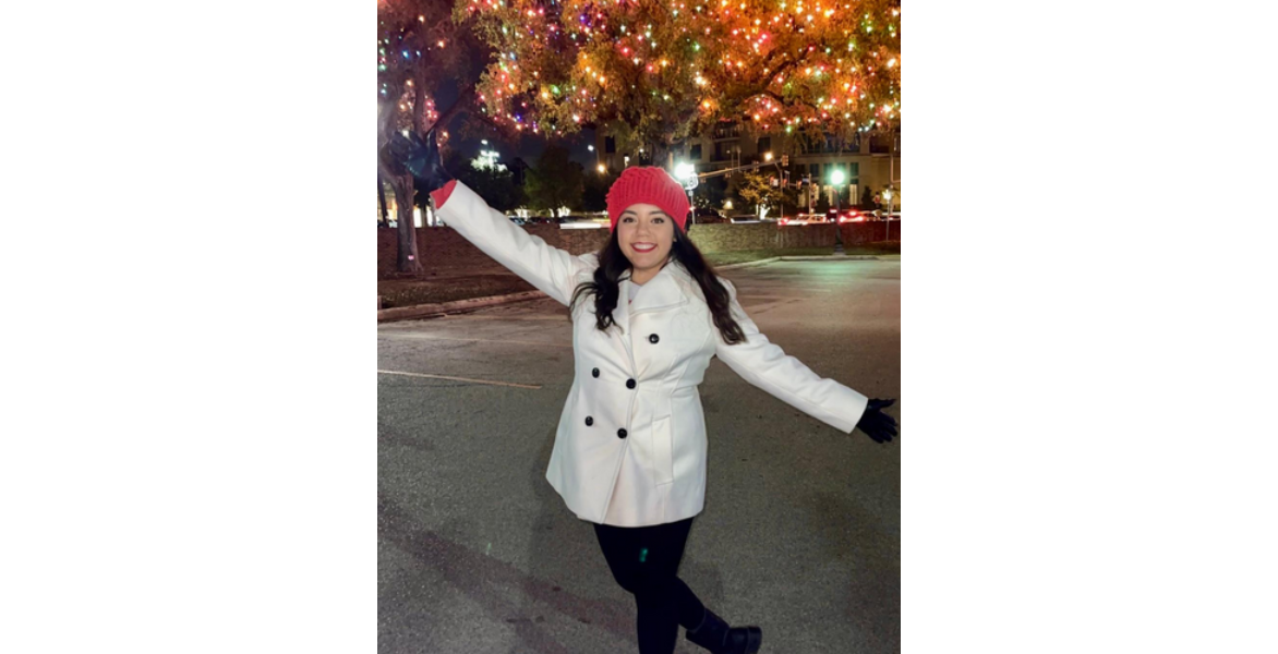 Woman in red hat and white coat poses with arms out