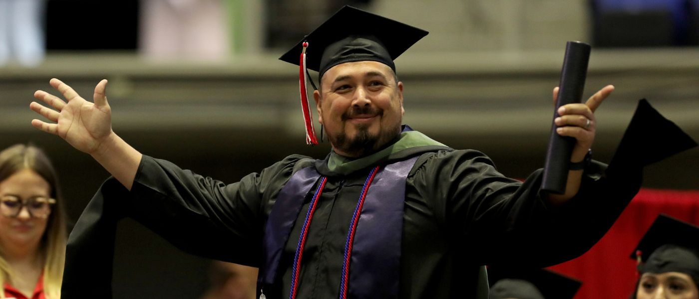 Student wearing cap and gown holds arms out in celebration