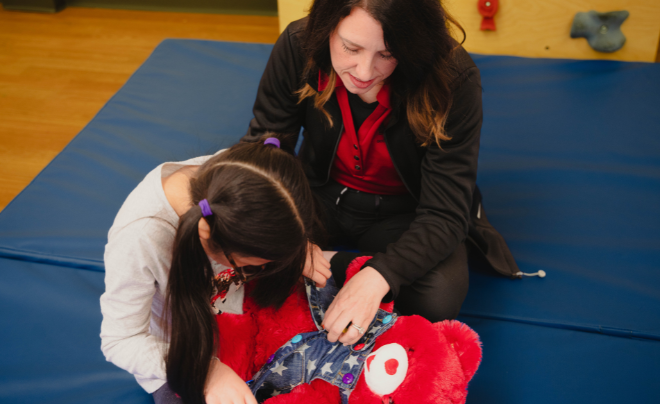 Child and physical therapist playing with a teddy bear