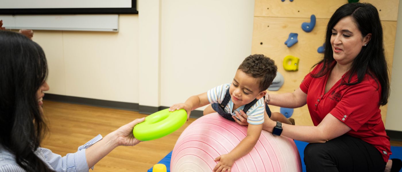 Child playing on exercise ball while a physical therapist holds his waist