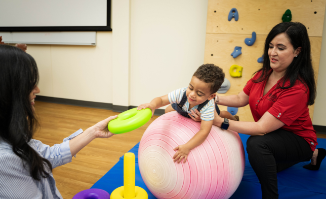 Child playing on exercise ball while a physical therapist holds his waist