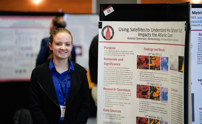 Student in blue top posing in front of poster