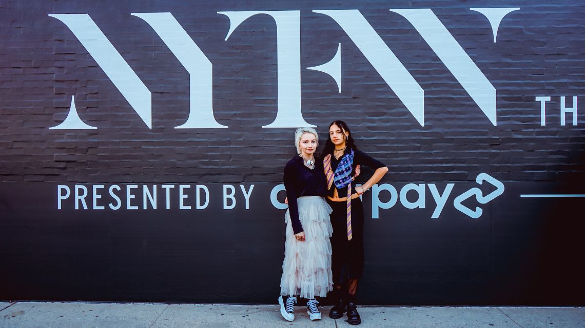 Sarah Cox and Maya Kanawati in front of NYFW sign