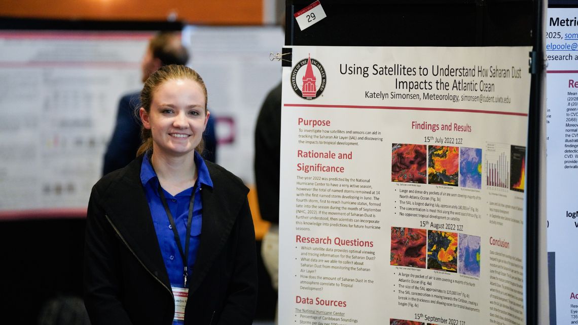 Student in blue top standing in front of a poster