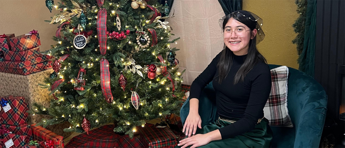 student sitting in front of a christmas tree with presents