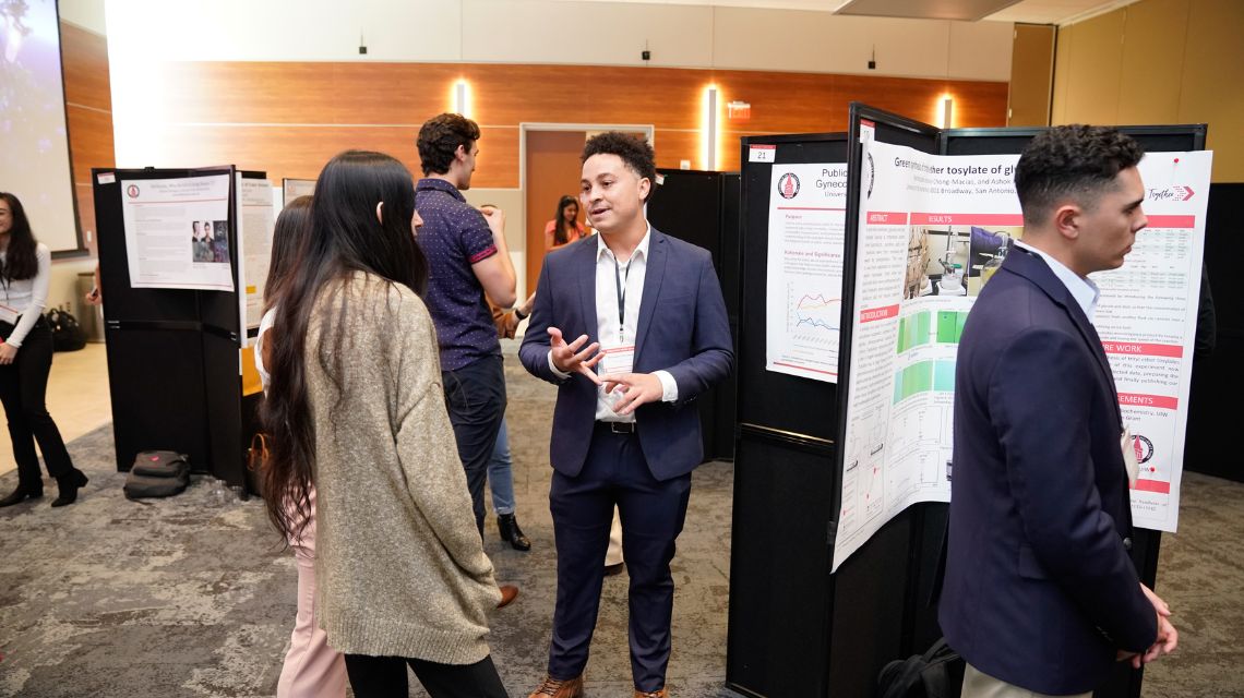 One student talking to two other students in front of a poster