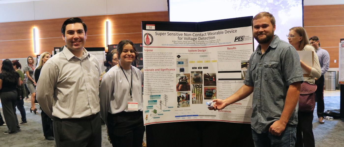 Three students smiling in front of poster