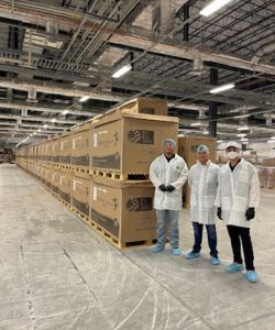 Three people in white lab coats next to boxes